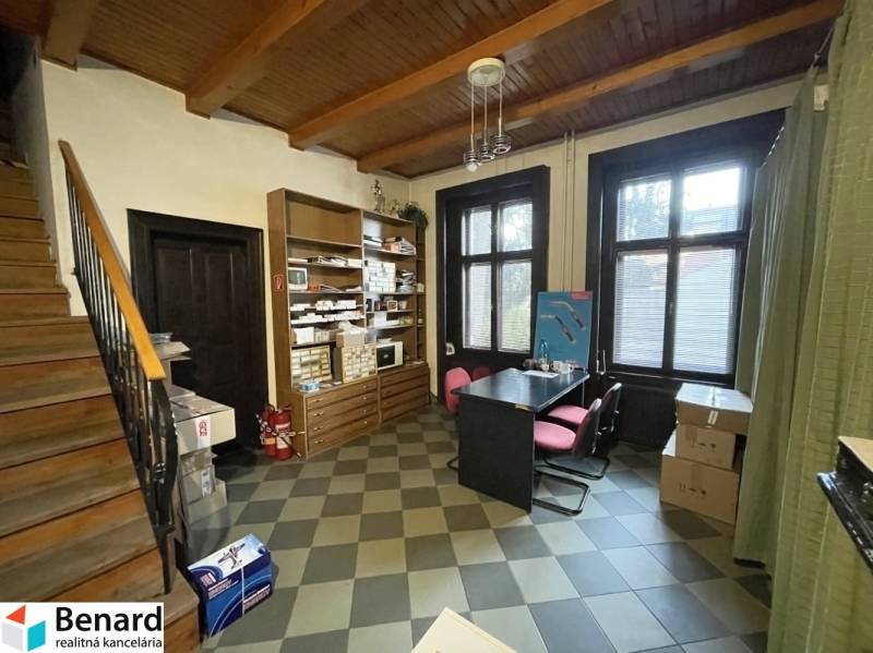 Ein Innenraum mit einer Holzdecke und einem dekorativen Boden, enthält einen Tisch mit Stühlen und Regale.