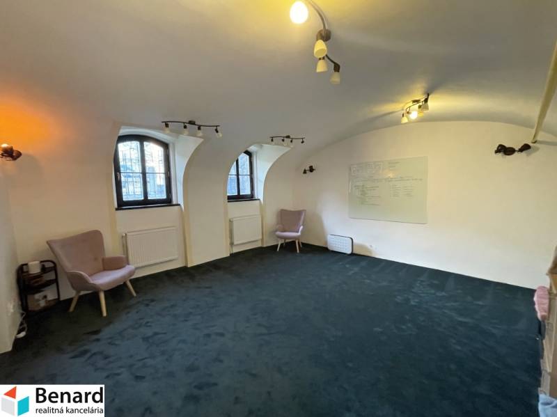 Interieur eines Gebäudes mit Bogenfenstern, grünem Teppichboden und Wandtafel.