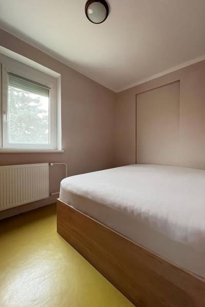 Schlafzimmer in einem Einfamilienhaus mit einfachem Bett, Fenster und Heizkörper.