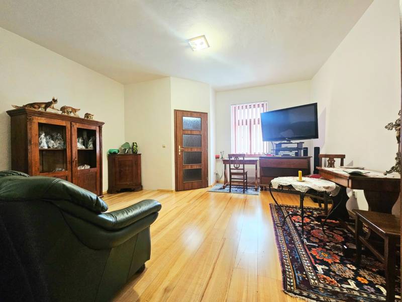 Wohnzimmer in einer 3-Zimmer-Wohnung mit Holzboden, ausgestattet mit einem Sofa und einem Fernseher.