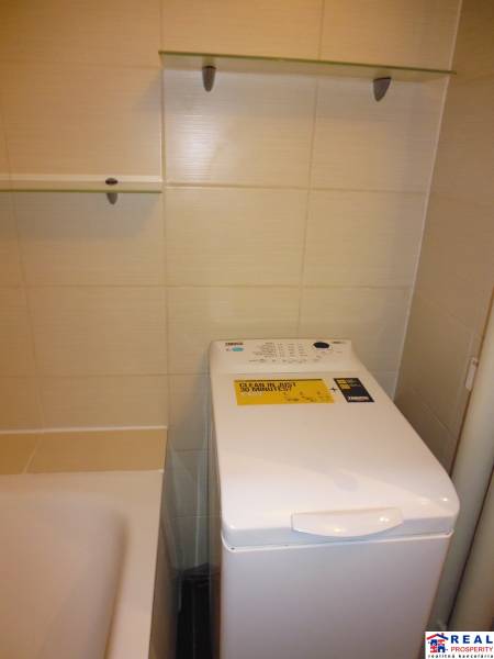 Badezimmer in einer 2-Zimmer-Wohnung mit Waschmaschine neben der Badewanne und Regalen.