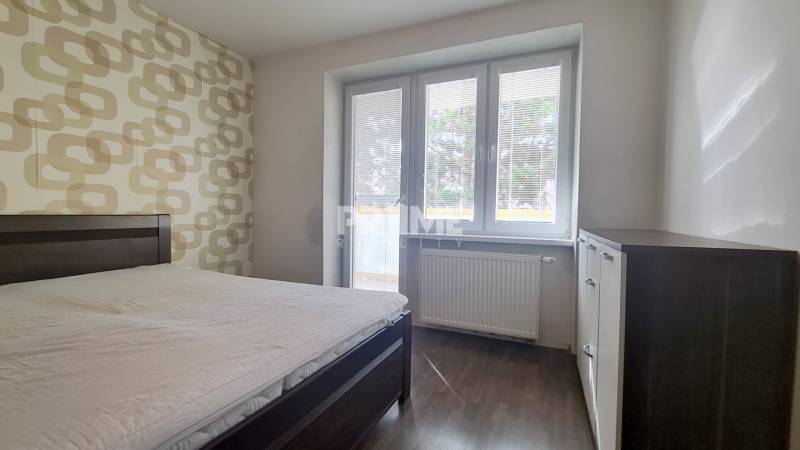 Schlafzimmer in einer 2-Zimmer-Wohnung mit Bett, gemusterten Tapeten und Boden in Holzoptik.
