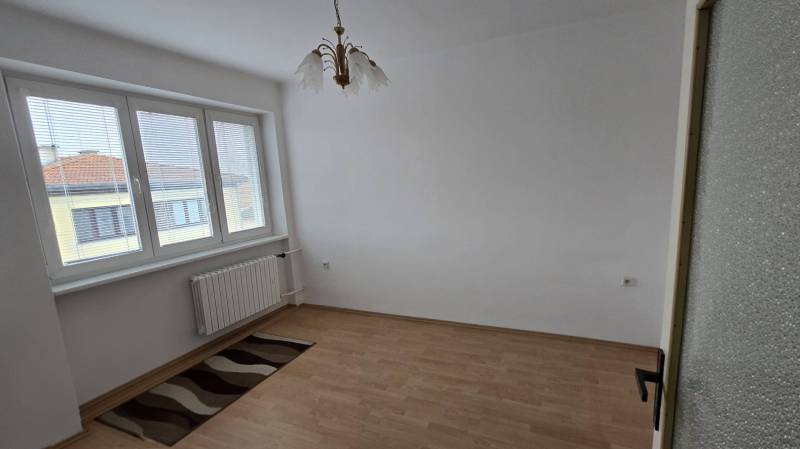 Ein Zimmer mit großen Fenstern, einem Boden in Holzoptik und einem Kronleuchter in einer 3-Zimmer-Wohnung.