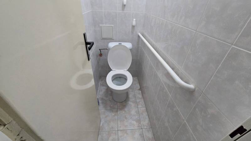 Badezimmer mit Toilette in einer 3-Zimmer-Wohnung, gefliest mit hellen Fliesen, mit einem Haltegriff an der Wand.