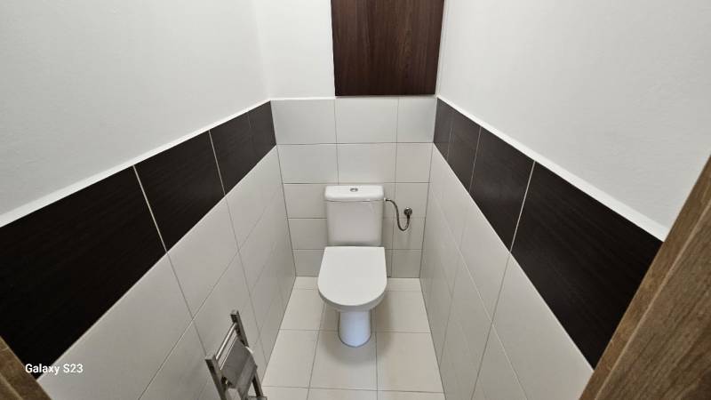 Toilette mit weißen Fliesen und dunklen Streifen in einer 3-Zimmer-Wohnung.
