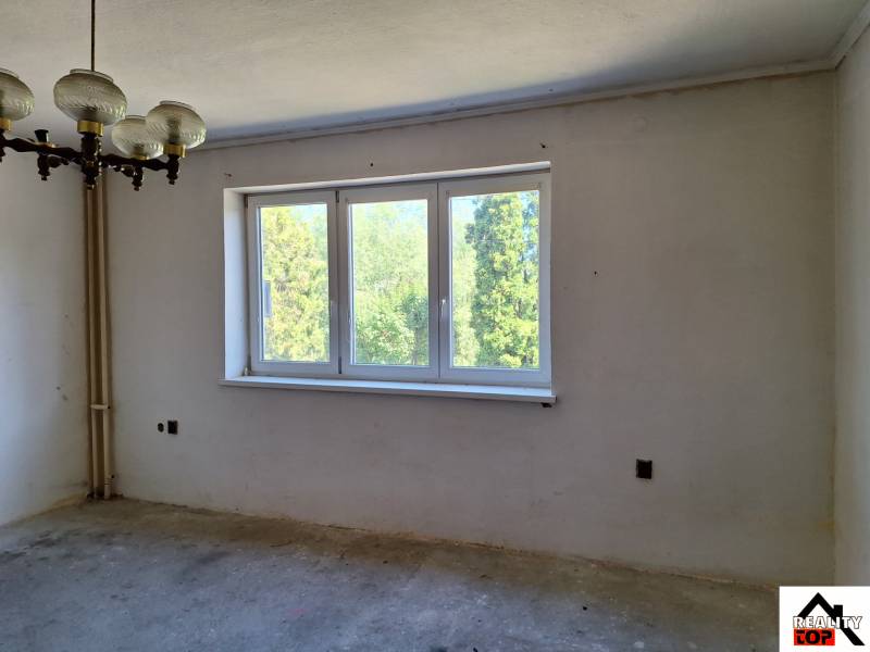 Ein Zimmer in einem Einfamilienhaus mit einem großen Fenster, einem originalen Kronleuchter und Blick ins Grüne.