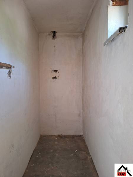 Ein enger Innenraum in einem Einfamilienhaus mit einem kleinen Fenster und Betonboden.