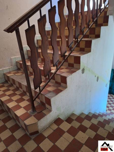 Eine Treppe mit einem Holzgeländer in einem Einfamilienhaus mit Fliesenboden.