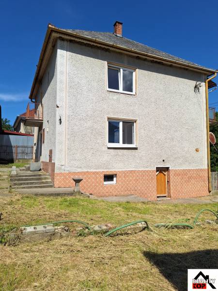 Ein Einfamilienhaus in Šíd mit einem steilen Dach und einem gepflegten Garten mit Rasen.
