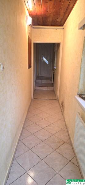 Ein schmaler Innenflur mit Fliesenboden und Holzdecke in einem Einfamilienhaus.