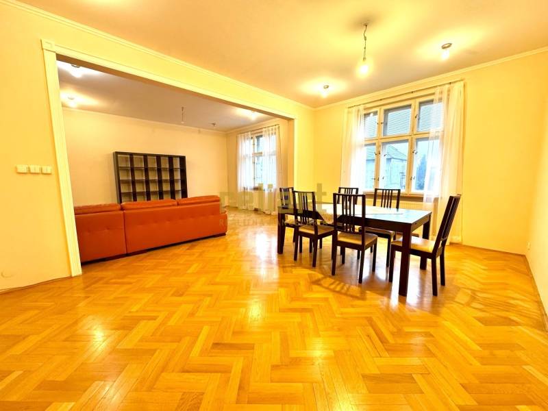 Esszimmer mit einem Tisch- und Stuhlset, neben einem Wohnzimmer mit einem orangefarbenen Sofa. Boden mit Holzdekor.