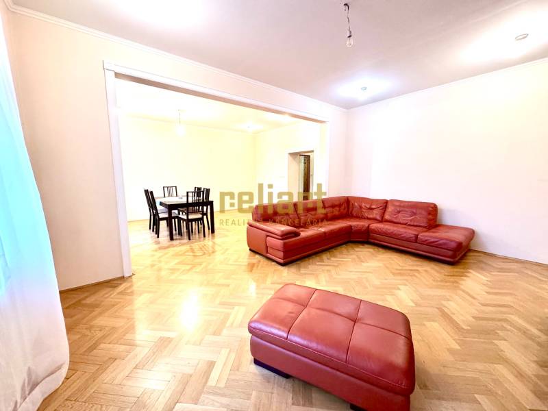 Wohnzimmer in einer Vierzimmerwohnung mit rotem Sofa und Holzboden.