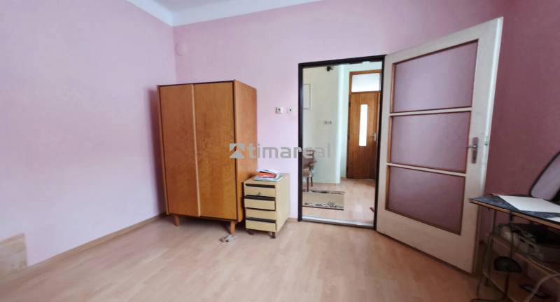 Ein Zimmer in einem Einfamilienhaus mit rosa Wänden, einem Boden in Holzoptik und Möbeln.