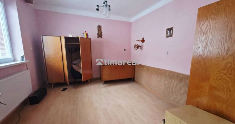 Ein Zimmer in einem Einfamilienhaus mit rosa Wänden, einem Kleiderschrank und einem Boden in Holzoptik.