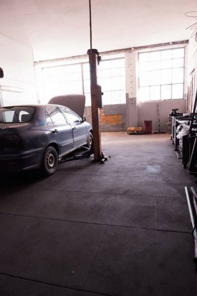 Ein Auto auf einem Hebebühne im Inneren eines Produktionsbereichs mit großen Fenstern.