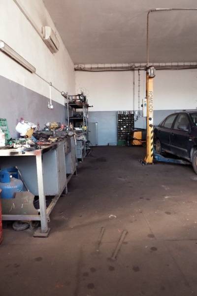 In der Werkstatt gibt es Werkzeuge, ein Auto auf dem Hebebühne und verstreute Teile auf dem Boden.