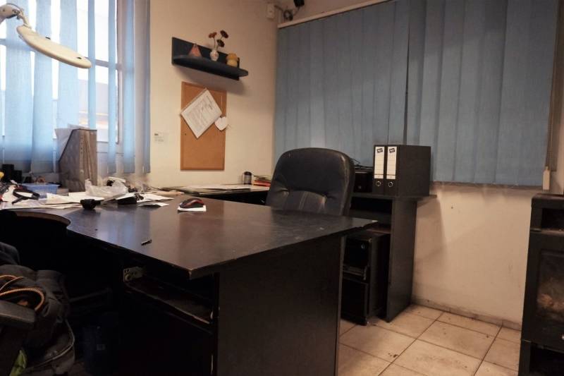 Ein Büro mit einem dunklen Tisch, Fliesenboden und blauen vertikalen Jalousien in einem Produktionsbereich.