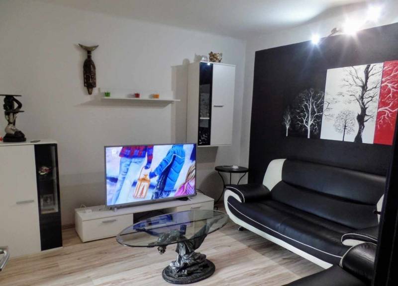 Wohnzimmer mit einem schwarz-weißen Sofa, Holzboden und Fernseher.