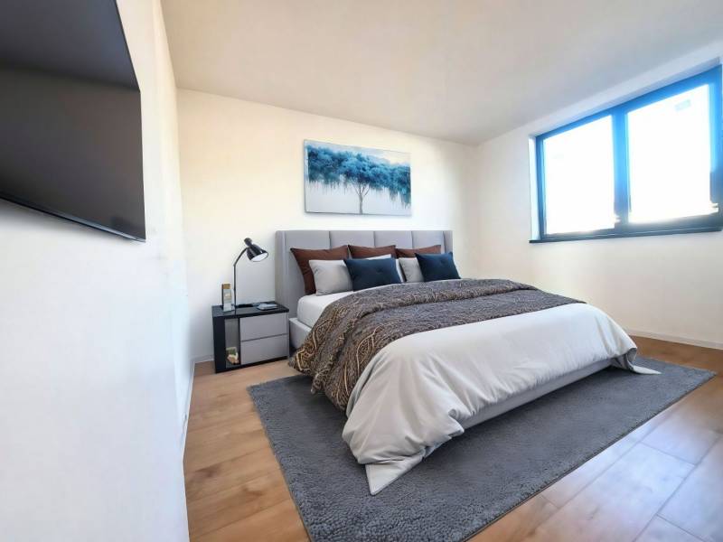 Schlafzimmer in einem Einfamilienhaus mit Bett, Bild, Fernseher und Boden in Holzoptik.