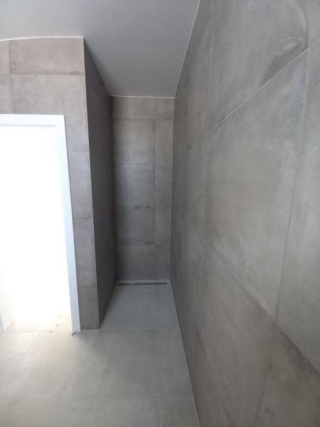 Ein Badezimmer in einem Einfamilienhaus mit großformatigen Fliesen und einer Duschzone ohne Duschwanne.