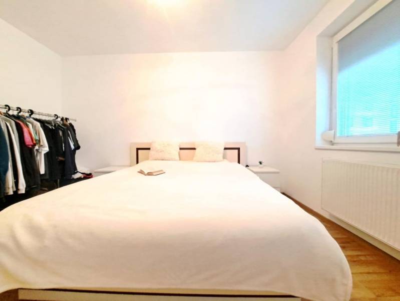 Schlafzimmer in einer 2-Zimmer-Wohnung mit Bett, offenem Kleiderschrank und Boden in Holzoptik.