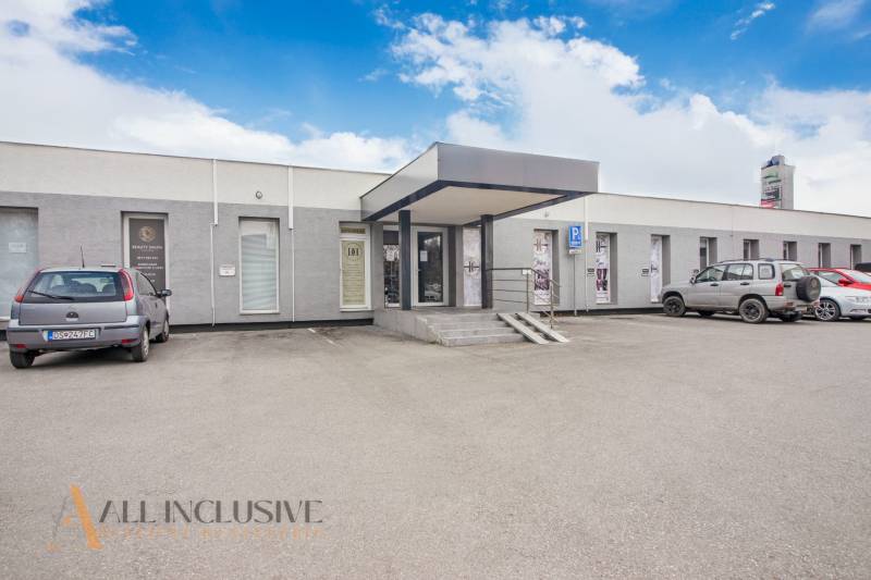 Einstöckiges Gebäude mit Geschäftsräumen in der Vajanského-Straße, Parkplatz und Autos vor dem Eingang.