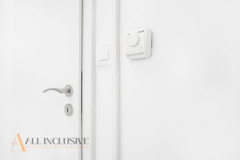 Weiße Wand mit Thermostat und Türklinke im Büro.