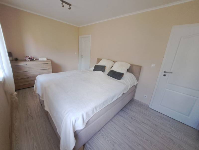 Schlafzimmer in einem Einfamilienhaus mit Bett, Kommode und Boden in Holzoptik.