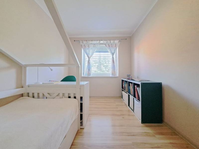 Ein Zimmer eines Einfamilienhauses mit einem Bett, einem Bücherregal und einem Boden mit Holzdekor.