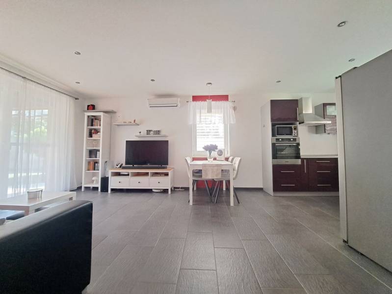 Wohnzimmer mit Fernseher, Küche und Esstisch, Boden mit Holzdekor.