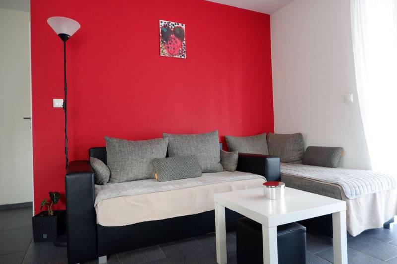 Innenraum eines Einfamilienhauses mit grauen Sofas, roter Wand und weißem Tisch.
