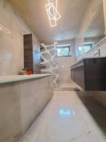 Ein Badezimmer in einem Einfamilienhaus mit Badewanne, moderner Beleuchtung, Fliesen und Waschbecken.