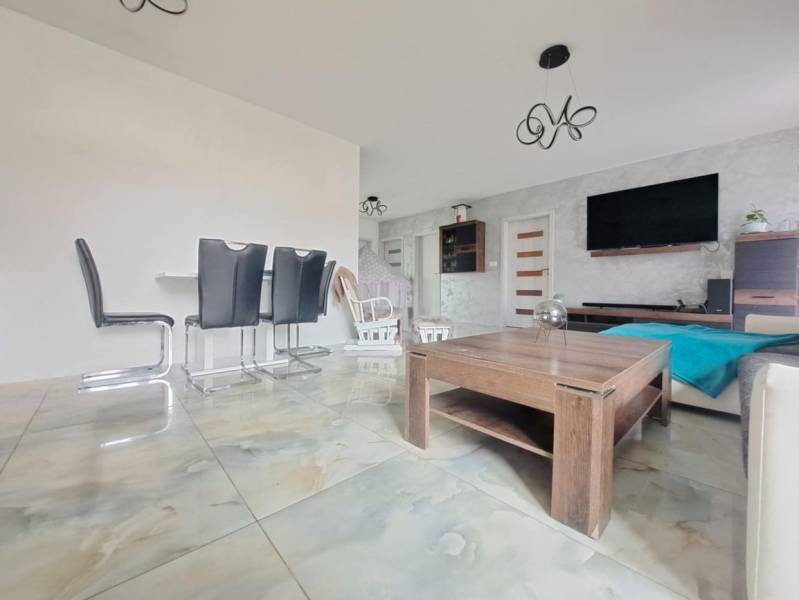 Innenraum eines Einfamilienhauses mit hellen Fliesen, modernen Möbeln und einer Wand mit Fernseher.