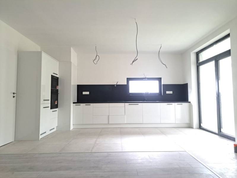 Küche in einem Einfamilienhaus mit Holzboden, weißen Schränken und eingebauten Geräten.