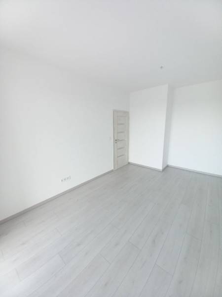 Ein Zimmer in einer 2-Zimmer-Wohnung mit weißen Wänden und einem Boden in Holzoptik.