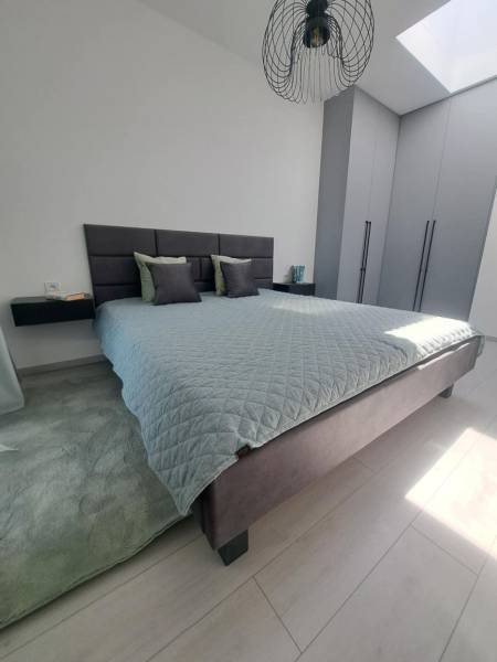 Schlafzimmer mit großem Bett, grauen Schränken und schwarzem Kronleuchter in einer 2-Zimmer-Wohnung.