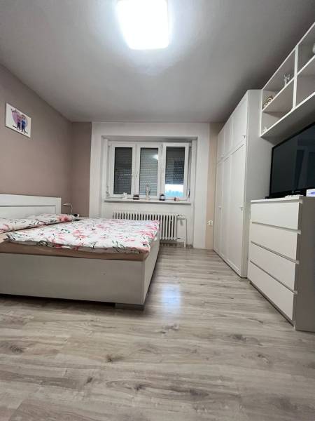 Helles Schlafzimmer in einem Einfamilienhaus mit Bett, Kleiderschrank und Boden in Holzoptik.