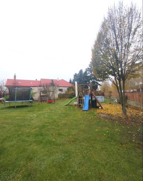 Ein Einfamilienhaus in Dunajská Streda mit einem Rasen im Garten, einem Trampolin und einem Kinderspielplatz.