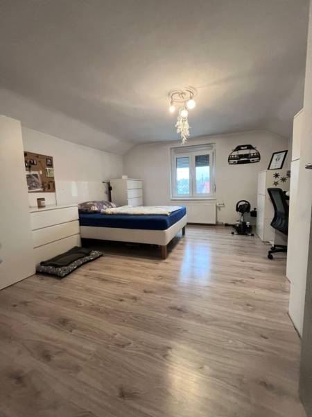 Ein Schlafzimmer in einem Einfamilienhaus mit einem Bett, weißen Möbeln und einem Boden in Holzoptik.