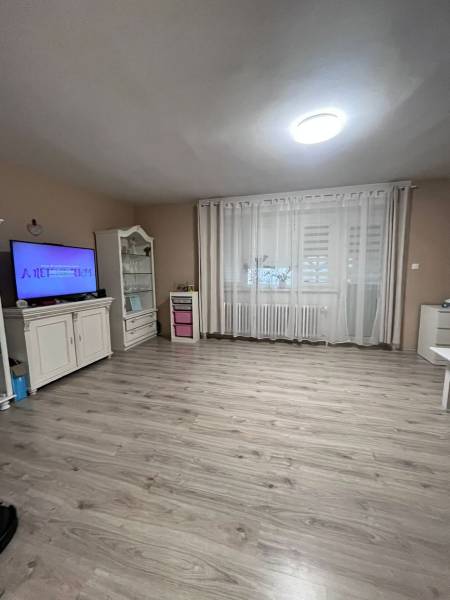 Ein Zimmer in einem Einfamilienhaus mit Holzboden, Fernseher und Vorhängen.