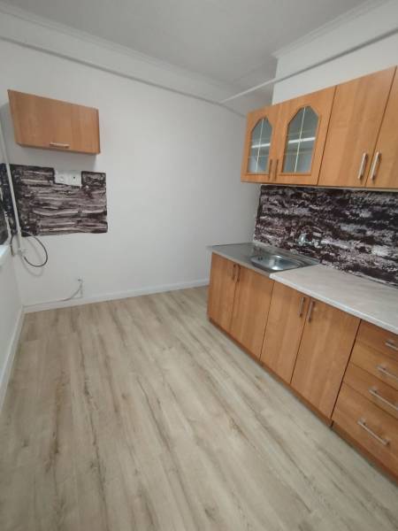 Die Küche in der 3-Zimmer-Wohnung hat einen Holzboden und einfache Schränke.