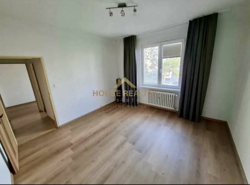Ein Zimmer in einer 4-Zimmer-Wohnung mit einem Boden in Holzoptik, Vorhängen, Heizkörper.