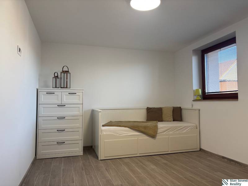 Ein Zimmer in einem Einfamilienhaus mit einem Bett, einer Kommode und einem Boden in Holzoptik.