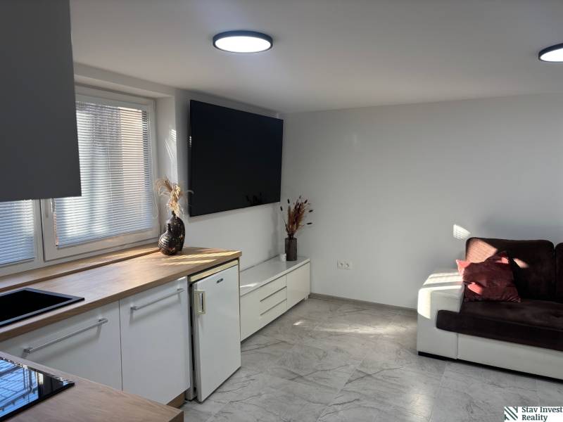 Wohnzimmer in einem Einfamilienhaus mit weißer Küchenzeile und dunkelbraunem Sofa.