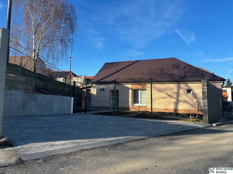 Ein Einfamilienhaus in Blatné mit einem braunen Dach, einem gepflasterten Parkplatz und einem Betonzaun.