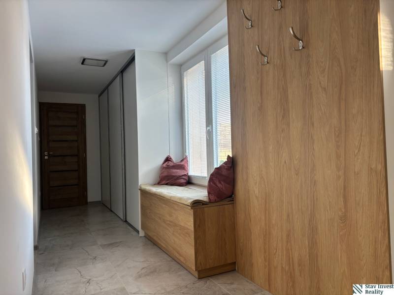 Flur in einem Einfamilienhaus mit Kleiderhaken und Sitzgelegenheit mit Kissen, Boden mit Holzdekor.