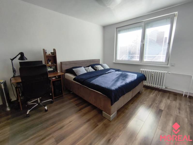 Ein Zimmer in einer Einzimmerwohnung mit einem Bett, einem Tisch und einem Boden in Holzoptik.