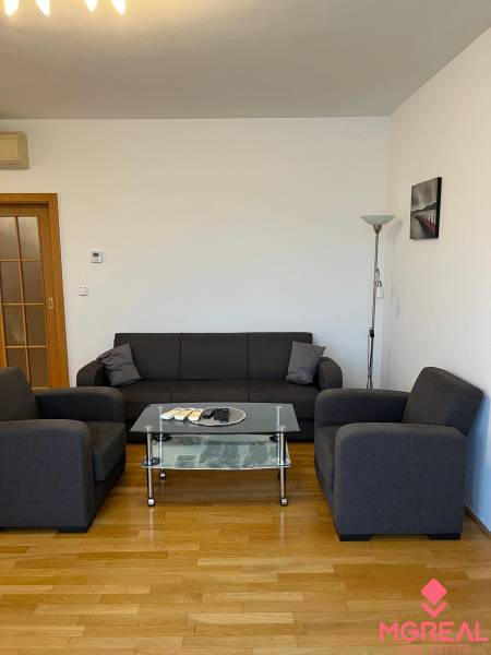 Graues Sofa in einer 3-Zimmer-Wohnung mit Holzboden und Glastisch.