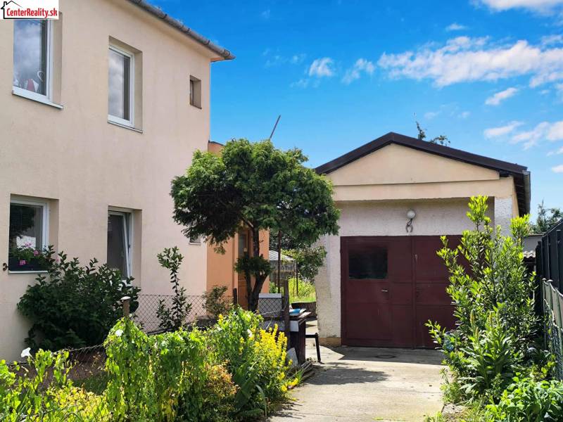 Ein Einfamilienhaus in Partizánske mit Garage, umgeben von einem Garten voller grüner Pflanzen.