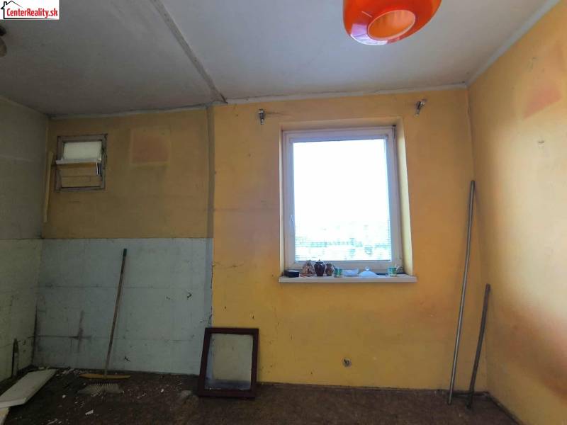 Ein Zimmer in einem Einfamilienhaus mit einem Fenster, einem Besen und orangefarbener Beleuchtung.